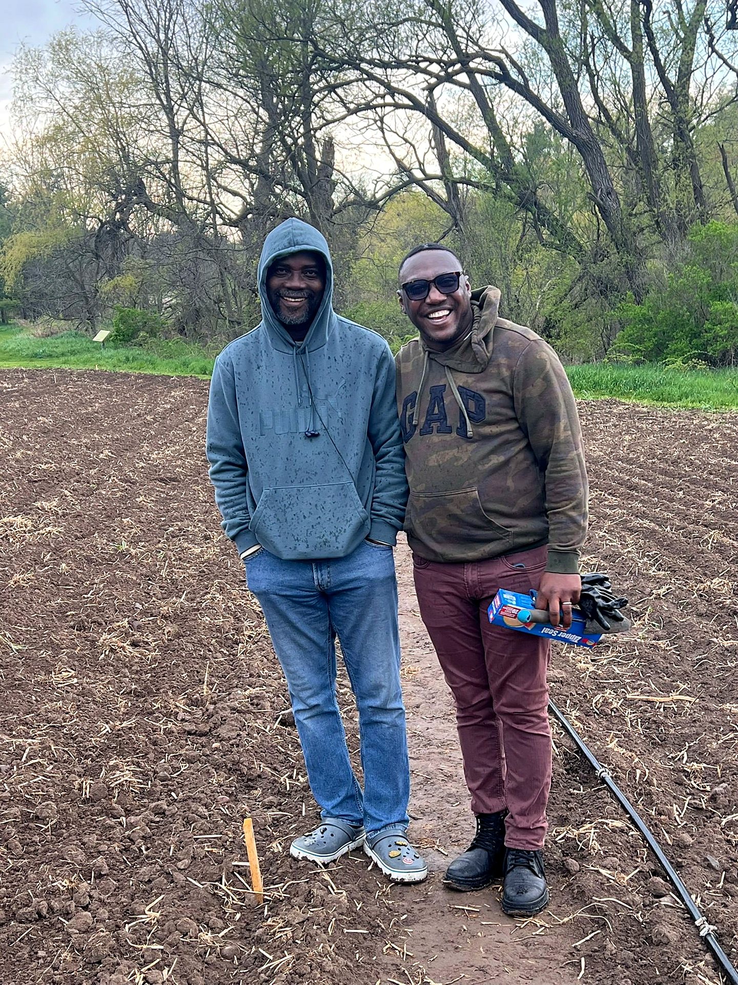 Two farmers smiling in freshly tilled spring beds before planting